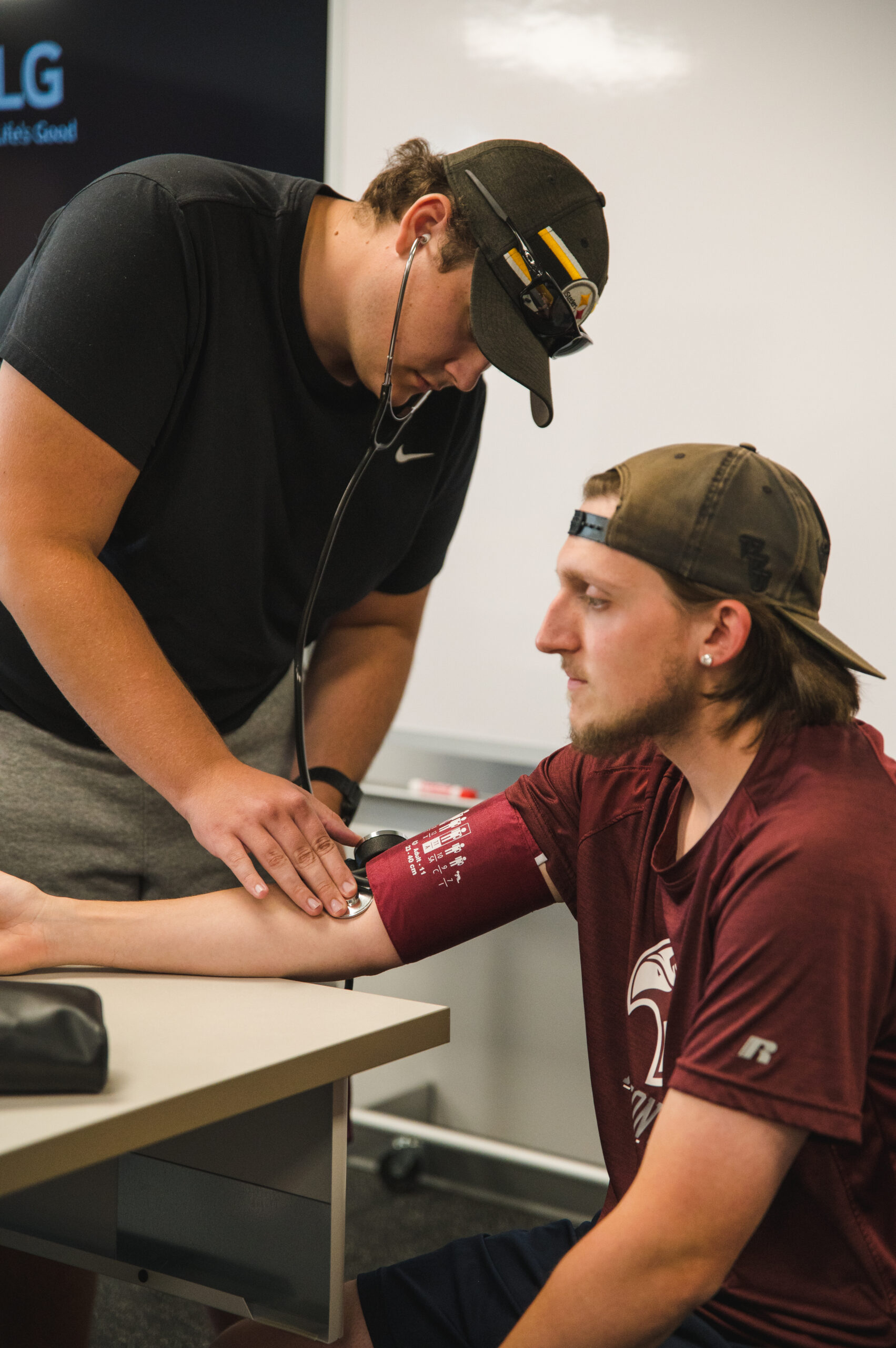 Student learning hands-on blood pressure measurement with peer guidance.
